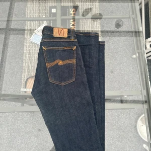 Nudie Jeans Skinny Lin – Rinsed Open Orange (W25 L32) - Supersnygga jeans från Nudie Jeans Co, modell Skinny Lin, i mörkblå denim med Nudies klassiska orangea sömmar. Smal passform med stretch som sitter perfekt! Tillverkade i 99% ekologisk bomull och 1% elastan – bekväma men hållbara. Använda väldigt lite, i riktigt fint skick 🌿  Storlek: W25 L32 Färg: Mörkblå (Rinsed Open Orange) Modell: Skinny Lin  Perfekta både till vardags och till en cleanare outfit ✨ 