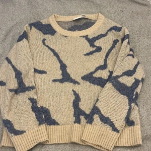 Beige stickad tröja med blått mönster - Säljer en beige stickad tröja från VILA i storlek XS. Använd ett fåtal gånger. Tröjan har ett fint blått camouflageinspirerat mönster och ribbade muddar vid hals, ärmslut och nederkant. Köpt för 400kr