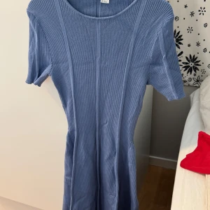 Blå ribbad kortklänning - Säljer en blå ribbad kortklänning med rund hals och korta ärmar. Klänningen har en slim passform och vertikala sömmar som ger en snygg siluett. Materialet är mjukt och stretchigt, perfekt för dig som gillar enkel och stilren design.