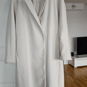 Creamfärgad  kappa från H&M i storlek S over size  - Stilren och lång creamfärgad kappa från H&M i storlek S. Klassisk design med krage, dolda knappar och raka ärmar. Perfekt för dig som gillar minimalistisk och clean look. Fickor på sidorna och mjukt material som känns skönt mot huden. Djur och rökfritt hem mycket bra skick 
