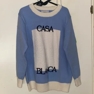 Ljusblå stickad tröja Casablanca storlek L - Snygg ljusblå stickad tröja från Casablanca Tennis Club i storlek L. Tröjan har kontrasterande vita muddar och krage, samt ett vitt fält framtill med svart broderad text 'CASA BLANCA'. Perfekt för dig som gillar stilrena och sportiga vibes.