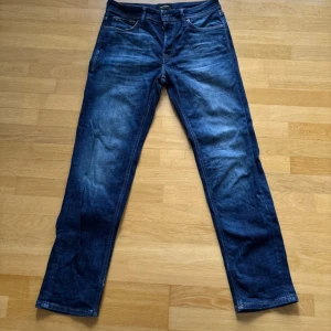 Blå jeans från Jack & Jones - Snygga blå jeans från Jack & Jones med klassisk femficksdesign och läderpatch bak i midjan. Jeansen har en rak passform och är tillverkade i slitstarkt denimtyg. Perfekta för dig som gillar en tidlös och enkel stil.