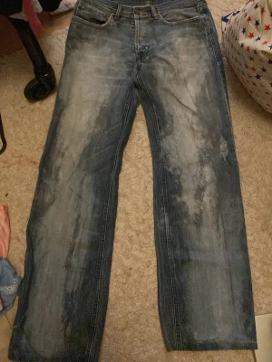 Blå jeansbyxor från Cross - Säljer ett par blå jeansbyxor från Cross med slitna detaljer och tvättad look. Klassisk femficksmodell med raka ben och kontrastsömmar. Materialet är robust jeans och färgen har en cool, blekt effekt som ger en avslappnad vibe.