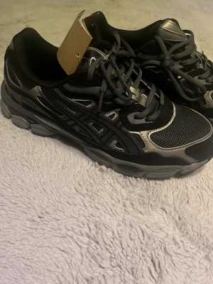 Asics gel nyc - Säljer ett par Asics gel nyc sneakers i storlek 42.5 med snygga detaljer i svart och silver. Med pris lappen på