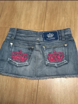 Victoria Beckham jeanskjol - Säljer en blå Victoria Beckham minikjol med rå kant och två bakfickor dekorerade med rosa broderade kronor🩷