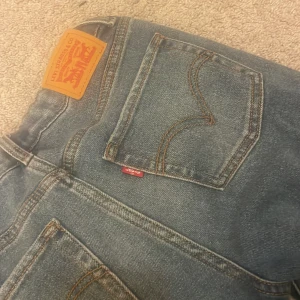 Levi's blå bootcut jeans - Säljer ett par klassiska Levis jeans i blå denim med bootcut passform. Färgen är en snygg mellanblå ton med vita detaljer på.