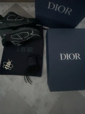 Svarta Dior B30 sneakers strl 43 - Säljer ett par svarta Dior B30 sneakers med vit och silver detalj på sidan och grov platt sula. Skorna har snörning och är tillverkade i microfiber mesh och syntetmaterial. Medföljer originalkartong, dustbag och extra skosnören och en Dior påse. Riktigt snygga och trendiga sneakers med tydlig Dior-logga. Önskas fler bilder får ni gärna skriva, priset kan möjligen diskuteras.