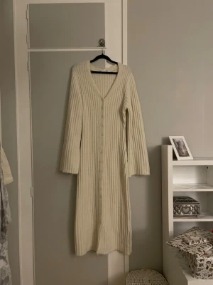 Beige stickad klänning  - Beige ribbad stickad maxiklänning med knappar längs med hela framsidan. V-ringad och är från Na-kd i storlek S. Köpt på Vinted med lappen kvar men säljer då den är för stor på mig