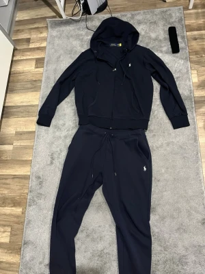 Polo Ralph Lauren Tracksuit - Snygga mörkblå mjukisbyxor från Polo Ralph Lauren med klassisk logga broderad på vänster ben. Byxorna har snörning i midjan, ribbade muddar vid benslut och är gjorda i mjukt bomullsmaterial. Perfekta för chill eller träning.