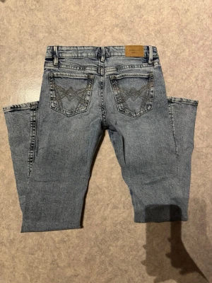 Perfekt Jeans ljusblå bootcut 34 - Säljer ett par ljusblå jeans från Perfect Jeans i storlek 34. Modellen har bootcut-ben och snygga broderade detaljer på bakfickorna. Klassisk femficksdesign med bälteshällor och knappstängning. Materialet är jeans med en mjuk känsla. Mått: 	•	Midjemått: ca 35 cm 	•	Grenhöjd: ca 18 cm 	•	Innerbenslängd: ca 77 cm