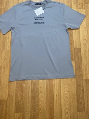 Grå   t-shirt XL - Snygg grå t-shirt  med svart tryck på bröstet. Klassisk rund hals och korta ärmar. Mjuk och skön bomullskvalitet som känns lyxig mot huden. Perfekt för dig som gillar stilrena designer och exklusiva märken.