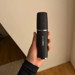 Tanrevel Pro Face Mist-enhet - Säljer en svart Tanrevel Pro Face Mist-enhet med silverdetaljer. Den är elektrisk och har en transparent behållare för vätska samt USB-port för laddning. Perfekt för att ge huden en fräsch och återfuktad känsla med ett jämnt mist-spray.