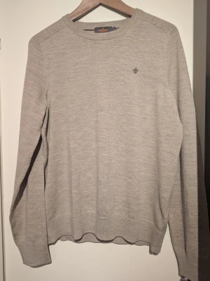 Stilren stickad tröja MORRIS nyskick! - Snygg beige stickad tröja från Morris med rund hals och diskret logga broderad på bröstet. Tröjan har långärmade ribbade muddar och är perfekt för lager-på-lager. Enkel och stilren design som passar till jeans eller chinos.