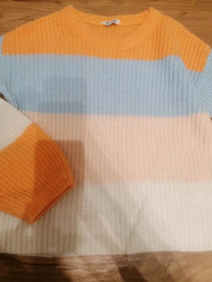Randig stickad tröja i pastell - Säljer en mysig stickad tröja från Cubus i storlek 158/164. Tröjan har breda ränder i orange, ljusblå, ljusrosa och vit, med rund hals och långärmad passform. Perfekt för dig som gillar färgglada och mjuka plagg med chill vibe. Den är lite noppig vid slutet av armarna, de bild nr. 5 😊