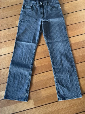 Viking Classic Style randiga jeans - Säljer ett par Viking Classic Style jeans med grå och svarta vertikala ränder. Modellen har raka ben, fem fickor och klassisk knappstängning. Materialet är jeans och byxorna har normal passform. Perfekt för dig som gillar retrovibe och tydliga detaljer.