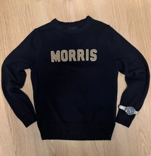 Marinblå stickad tröja från Morris - Marinblå stickad tröja från Morris. Rund halsringning och ribbade muddar vid ärmslut och nederkant. Perfekt för dig som gillar stilrena och klassiska plagg med tydlig branding.