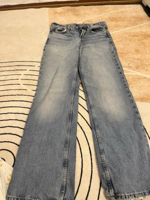 Jeans Zara - Säljer ett par blå jeans med ljus tvätt och breda ben från Zara. Klassisk femficksmodell med knapp och dragkedja framtill. Jeansen har en avslappnad passform och är tillverkade i jeansmaterial. Perfekt för dig som gillar en chill och trendig stil.