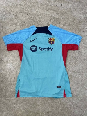 Ingen sko på bilden - Bilden visar ingen sko, utan en fotbollströja från FC Barcelona med Nike-logga och Spotify som sponsor. Tröjan är ljusblå med röda detaljer och klubbmärke på bröstet.
