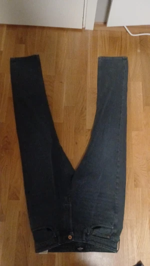 Svarta straight jeans från Levi's - Säljer ett par svarta jeans från Levi's med klassisk femficksdesign och rak passform. Jeansen har en mörk tvätt och Levi's läderpatch baktill i midjan. Materialet är slitstarkt denim i bomull och de har knappstängning framtill. 30/34 