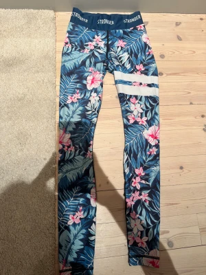 Blommiga leggings från Stronger - Snygga leggings från Stronger i storlek XS med tropiskt blommigt mönster i blått, rosa och vitt. Stretchigt material i polyester och elastan. Perfekta för träning och ger en skön vibe till din outfit. Passar från 10-13 år.