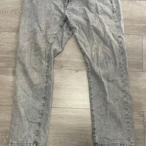 Grå jeans från Woodbird, storlek 32/30 - Snygga grå jeans från Woodbird i modellen Doc Ash. Jeansen har en klassisk rak passform och är tillverkade i ekologisk bomull. De har en cool tvättad look och passar perfekt till streetwear eller en avslappnad stil. 