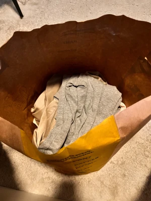 En till full påse med massa kläder i! - I denna påse full med kläder finns det en rosa mjuk tröja med litet tryck på franska från lager 157 i storlek M,  en tight T-shirt med urigning från lager 157 i storlek S, ett par mjukis byxor i grå färg från lager 157 i storlek M, en beige tunn hoodie från Gina tricot i storlek S, en beige tunn stickad tröja från lager 157 i storlek S, ett par svarta mjukis byxor från lager 157 i storlek S.