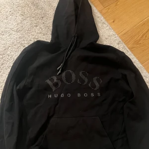 Svart Hugo Boss Hoodie - Svart hoodie från Hugo Boss i storlek M med stor BOSS-logga. Pris kan sänkas vid snabb affär. Hör av dig vid intresse eller liknande😁
