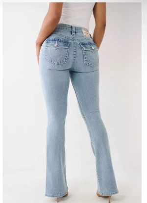 Ljusblå bootcut jeans från True Religion - Snygga ljusblå jeans från True Religion med klassiska fickor och dekorativa sömmar bak. Modellen har bootcut-ben och låg midja, vilket ger en cool och avslappnad vibe. Jeansen är tillverkade i mjukt denim och har silverfärgade detaljer vid fickorna.