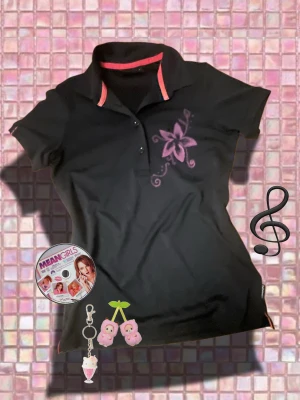 Svart pikétröja Peak Performance S - Svart pikétröja från Peak Performance i storlek S. Tröjan har en lila blommig print på bröstet och snygga röda detaljer på kragen. Klassisk pikémodell med korta ärmar och knappar framtill. Perfekt för dig som gillar sportig och chill stil.