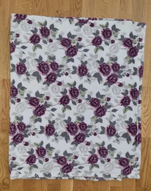 Vit blommig fleecekjol - Mysig vit kjol med blommigt mönster i lila och grå toner. Kjolen är rak i modellen och tillverkad i mjuk fleece, perfekt för dig som gillar en bekväm och söt stil. Blommorna har detaljer i grönt och rosa för en extra färgklick. Mått:125×150.