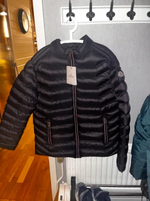 Svart Moncler dunjacka med dragkedja - Hjälper min pappa sälja sin moncler jacka.  Helt ny har bara blivit liggandes i garderoben! Skicka gärna hur ni vill ha bilderna om ni vill ha fler bilder!