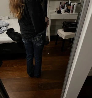 Mörkblå Miss Me jeans med kontrastsömmar - Snygga mörkblå jeans från Miss Me med vita kontrastsömmar och detaljerade bakfickor med metallknappar. Jeansen har en klassisk straight passform och låg midja, samt slitningar framtill för en cool look. Perfekt för dig som gillar statement-jeans.