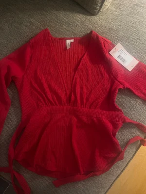 Röd topp med knyt  - Säljer denna superfina topp från Nelly❤️ Säljer då den inte har kommit till användning, lappen är kvar. Finns inte kvar på hemsidan längre. Den har knyt i midjan som ger en bra passform, perfekt till jul!❤️❤️ Kan gå ner i pris vid snabb affär❤️