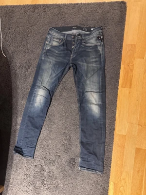Replay Anbass slim jeans blå - Säljer ett par Replay Anbass jeans i mörkblå tvätt med snygga slitningar och kontrastsömmar på bakfickorna. Modellen är skinny med låg midja och klassisk femficksdesign. Perfekt passform för dig som gillar smalare jeans.