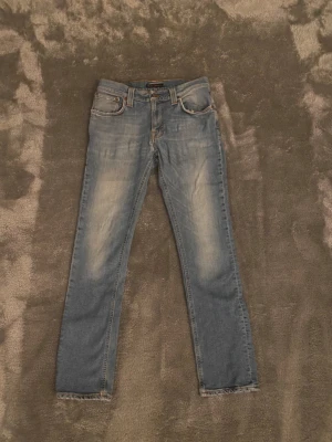  Nudie Jeans - Snygga blå jeans från Nudie Jeans, tillverkade i 100% ekologisk bomull. De har klassisk femficksdesign och ljusare tvättade partier. De har ett litet hål som syns på bilden men är lätt att laga. W32 L32