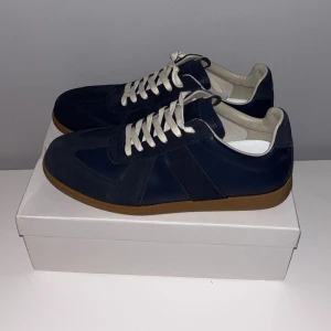 Maison Margela sneakers i marinblå mocka - Maison Margela sneakers i marinblå mocka och skinn med vita snören och klassisk gummisula. Snygg retrostil med rund tå och låg profil. 