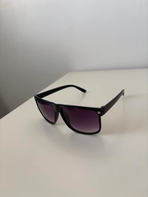 Raybans boyfriend liknande - Snygga solglasögon med svart, fyrkantig ram och lila tonade glas. Modellen har breda skalmar och en modern, stilren look som passar dig som gillar att sticka ut. Ramen är i plast och glasen har en cool gradient från mörkt till ljusare lila. Helt nya.