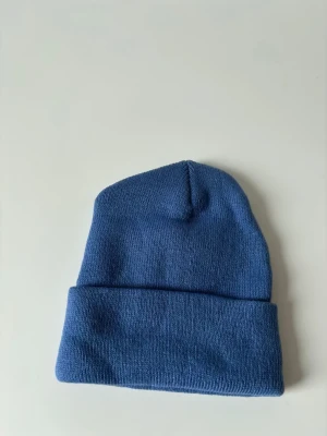 Blå stickad mössa  - En stilren blå mössa med klassisk uppvikt kant. Stickad i mjukt material som håller dig varm och passar perfekt till kyliga dagar. Enkel design som funkar till alla outfits och ger en chill vibe. Helt ny.