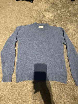 Blå merinoulltröja från Valient - Snygg blå merinoulltröja från Valient, använd fyra gånger och blivit tvättad en gång. Tröjan har en klassisk, enkel design och är långärmad, perfekt för att hålla dig varm och stilren under kyliga dagar. Nypris: 699kr 