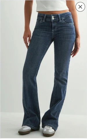 Blå bootcut Nelly - Snygga blå bootcut jeans med låg midja från Nelly. Jeansen har vita broderade detaljer på bakfickorna och dubbla knappar i midjan. Tillverkade i mjukt denimtyg som ger en bekväm passform. 