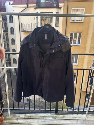 Mörkblå vindjacka Tommy Hilfiger M - ⭐️⭐️⭐️Snygg mörkblå jacka från Tommy Hilfiger i storlek M. Jackan har en bortagbar luva och snygg diskret logga på ärmen. Liten defekt på insidan av jackan men påverkar inte. Riktigt snygg och passar perfekt med en tröja till årets vinter. ⭐️⭐️⭐️