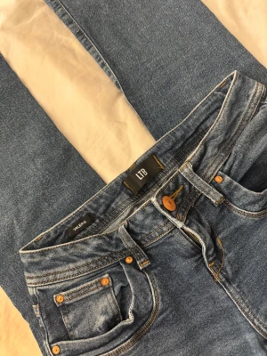 Blå jeans från LTB, modell Valerie - Snygga blå jeans från LTB i modellen Valerie. Klassisk femficksdesign med kopparfärgade nitar och knapp. Jeansen har en rak passform och är tillverkade i jeansmaterial med tydliga sömmar. Perfekt för dig som gillar en enkel och stilren look.