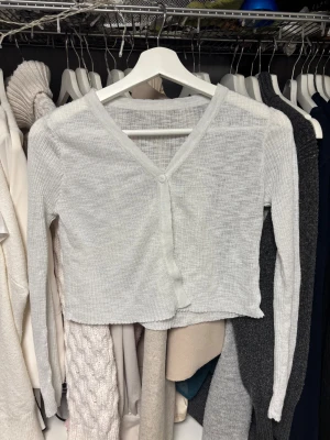 Vit ribbad kofta - Koftan har en knapp framtill och är tillverkad i ett lätt, stickat material.