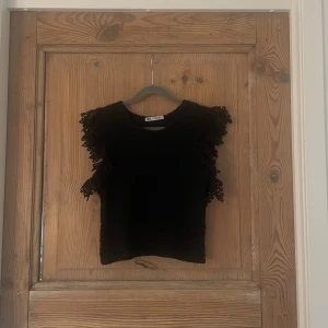 Svart blus med spetsvolanger från Zara - Supersnygg svart blus från Zara med coola spetsvolanger på axlarna. Den är använd få gånger och i super fint skick🩷