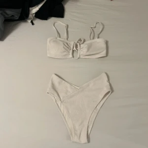 Vit bikini med snörning från H&M - Superfin vit bikini från H&M! Ett par helfodrade bikinitrosor med hög, V-skuren midja och snedställd söm fram och bak. Trosorna är halvtäckande bak. Och en fodrad, bygellös bikini-bh med reglerbara axelband. Bh:n har kupor med uttagbara inlägg som formar bysten och ger bra stöd. Stödskenor i sidorna och öppning i mitten på bysten med smal dragsko med dekorativa metallhängen i ändarna. Saknar knäppning! Plaggen har använts endast en gång och kostade 467 kr! Både plaggen är storlek S.