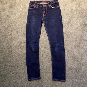 Mörkblå skinny jeans från Nudie Jeans - Säljer ett par mörkblå skinny jeans från Nudie Jeans i modellen Skinny Lin. Klassisk femficksdesign, orangea kontrastsömmar och stretchigt jeanstyg för en tight passform. Perfekta för dig som gillar en smal siluett och stilren look.GYLFEN ÄR SÖNDER!!