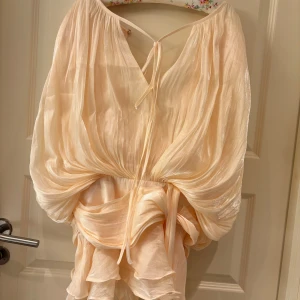 Krämvit omlottklänning med knytband - Superfin krämvit klänning i glansigt material med voluminösa, långa ärmar och bred midjedel med knytband. Blusen har omlottkänsla, lätt plissering och v-ringning med knyt framtill. Klänningen är helt ny med prislapp kvar. Orginalpris är runt 1500 kr men jag säljer för 1000 kr. Hör av er om ni har några frågor eller funderingar!💗💗