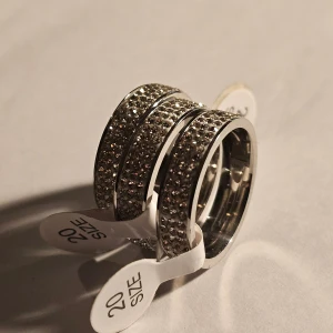 Glittriga silverringar storlek 20 - Tre snygga silverfärgade ringar i storlek 20, täckta med glittrande stenar runt hela bandet. Rostfritt stål, alla är ca 19.8 mm