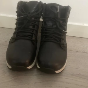 Svarta vattentäta boots från Everest  - Svarta boots från Everest med vattentätt material och snörning framtill. Skorna har en vit, mönstrad sula och vadderad kant i textil upptill för extra komfort. Perfekta för höst och vinter när du vill hålla fötterna torra och varma.