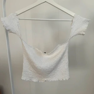 Söt vit topp med smockat tyg - Söt vit topp med smockat tyg och off-shoulder-design. Stretchig och bekväm i storlek S. Använd en del men är i fortsatt bra skick. Har en knappt synbar minimal fläck på insidan av tyget (se bild), dock inget som syns utanpå när man har plagget på sig. Köpt på Nelly.